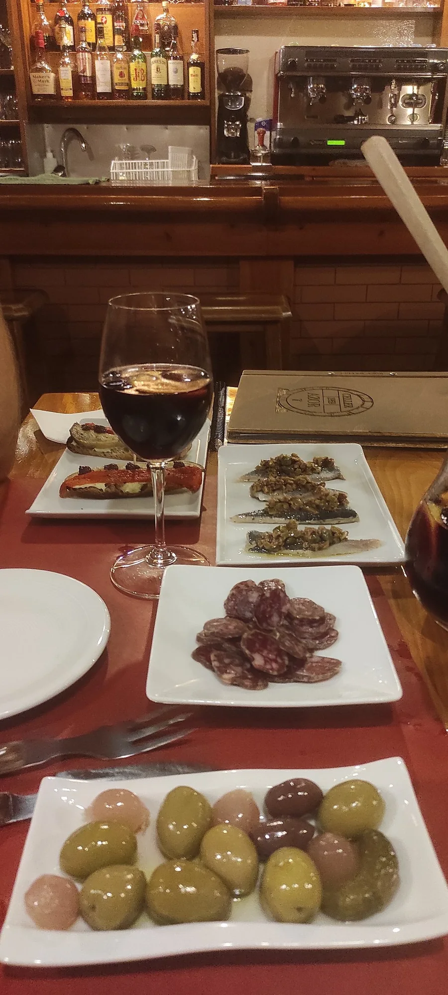 Copa de vino con torradas, sardinas y embutidos en la barra